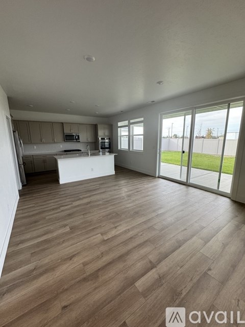 A spacious living room with wooden flooring and a kitchen area in the background.