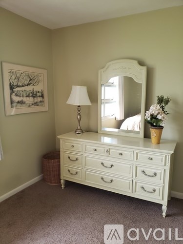A white vanity with a mirror, lamp, and flowers.