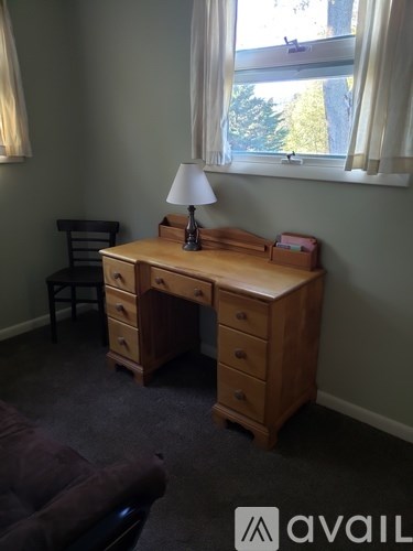 A wooden desk with drawers and a chair in front of a window.
