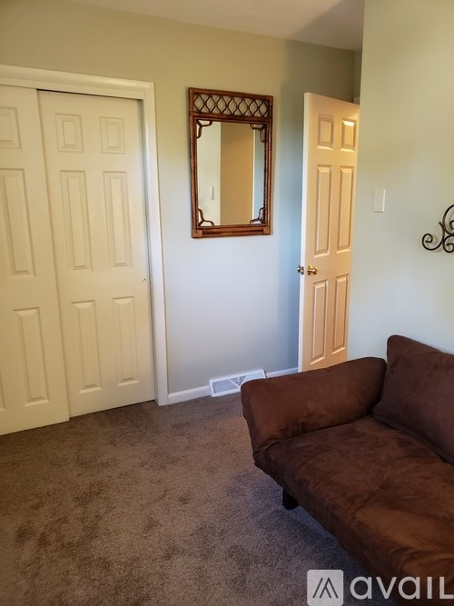 A brown couch sits in a room with a mirror and two doors.