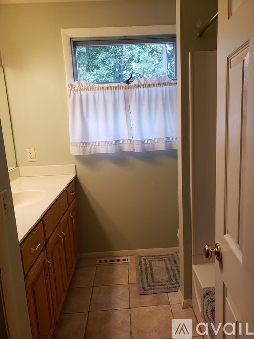A bathroom with a window covered by a white curtain.