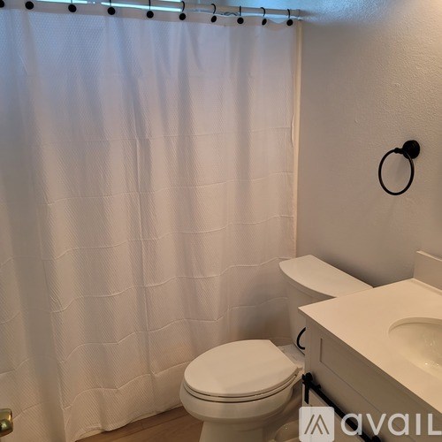 A white toilet in a bathroom with a white shower curtain.