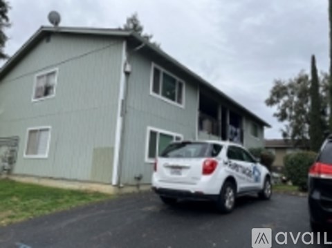 A white car is parked in front of a grey house.