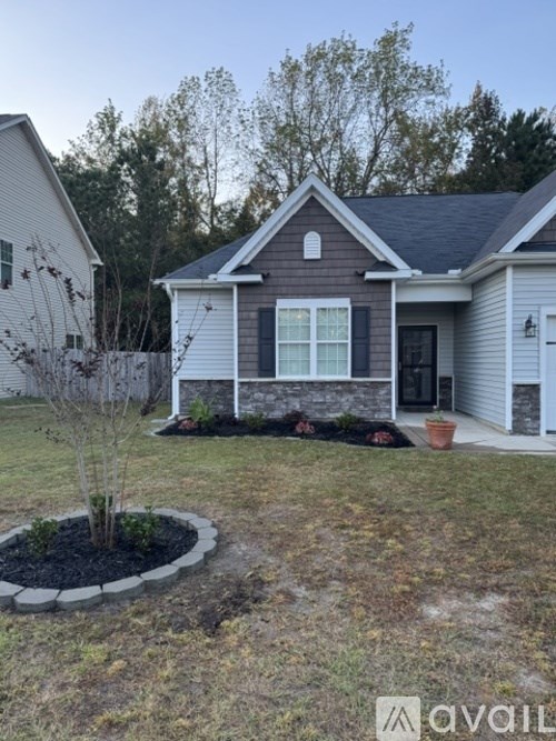 A house with a grey roof and a small tree in a circular flower bed.