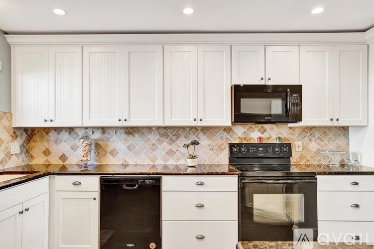 A kitchen with white cabinets and a black microwave above the stove.