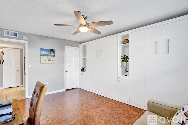 A living room with a ceiling fan and a painting of a beach scene on the wall.