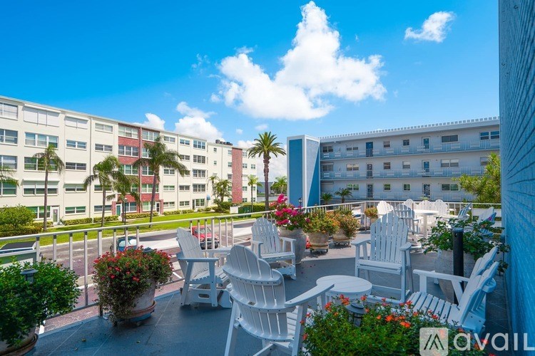 A balcony with white chairs and tables overlooks a courtyard with plants and buildings.