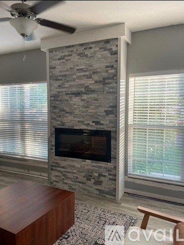A room with a stone fireplace and a ceiling fan.