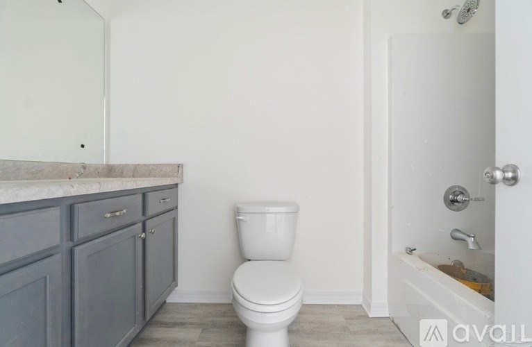 A white toilet sits in a bathroom with a grey cabinet and a bathtub with a shower head.