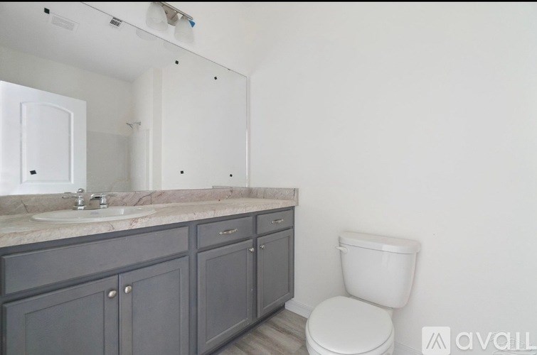 A bathroom with a toilet, sink, and cabinets.