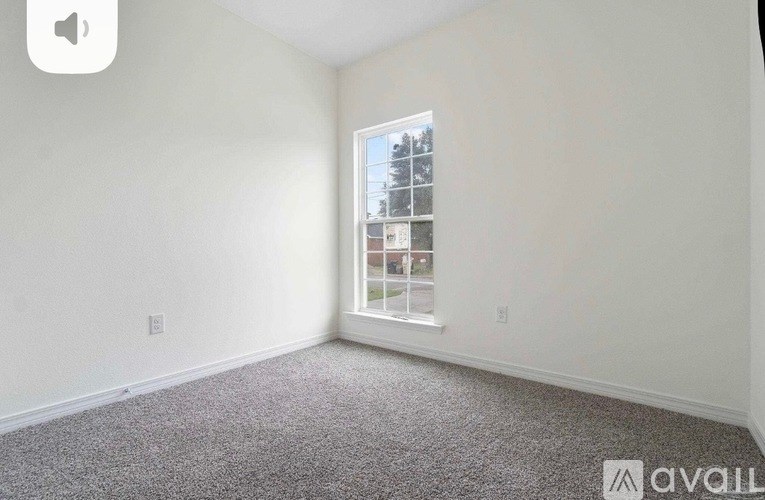 A room with a carpeted floor and a window showing a view of a building and trees outside.