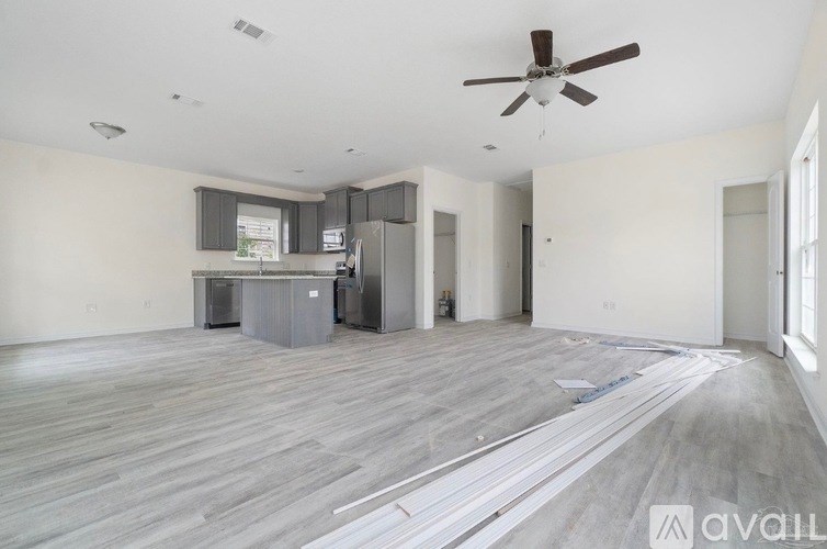 A spacious living room with a kitchenette and a ceiling fan.