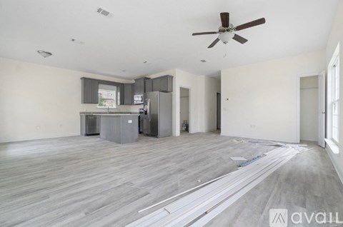 A spacious living room with a kitchenette and a ceiling fan.
