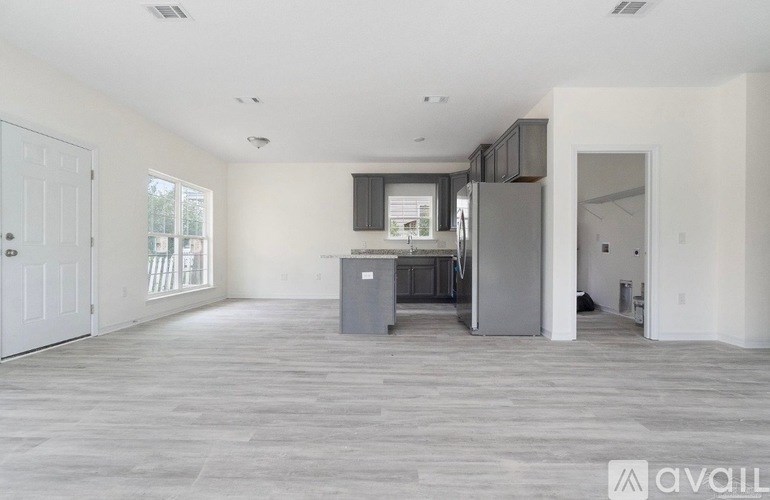 A spacious, empty room with a kitchen area in the background.