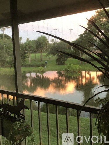 A balcony view of a pond with trees and a house in the background.