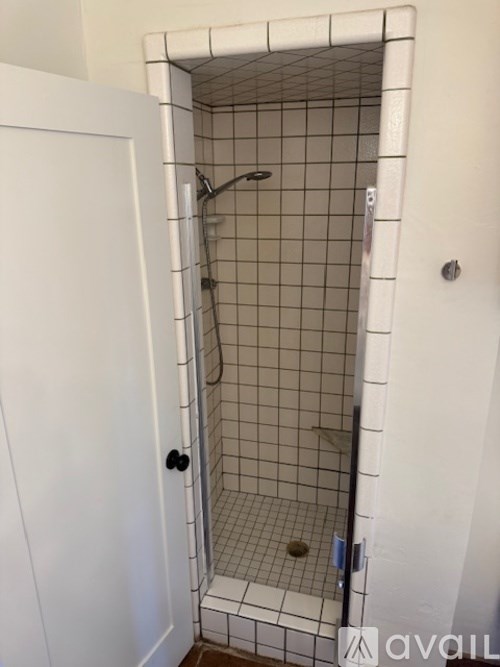 A white door is open to a shower with a white tiled wall.