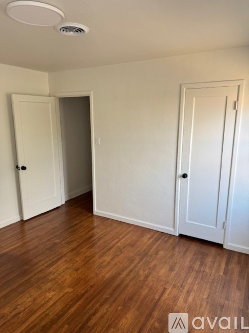A room with wooden floors and white walls, with a ceiling light and two doors.