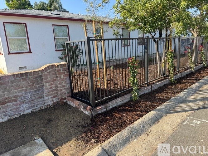 A white house with a black fence and a tree in front.