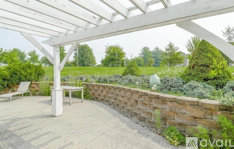 A patio with a white pergola and a stone wall.