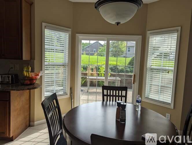 A dining room with a table, chairs, and a view of the backyard through the windows.