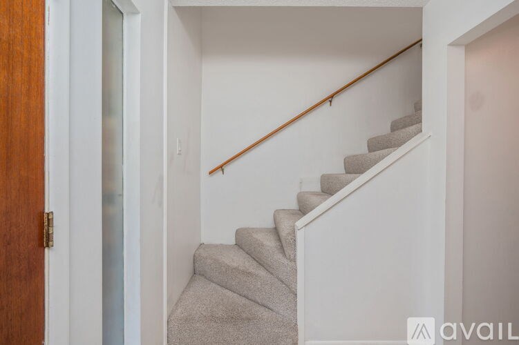 A staircase with a wooden handrail and beige carpeted steps.