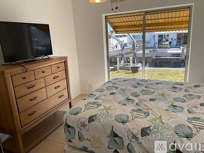 A bedroom with a bed, a television, and a window overlooking a patio.