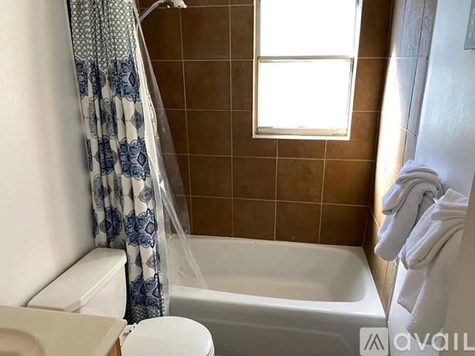 A bathroom with a white toilet, a bathtub with a shower curtain, and a window.