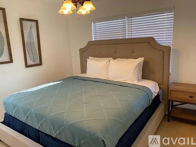 A bed with a blue quilt and white pillows is in a room with a chandelier and two framed pictures on the wall.