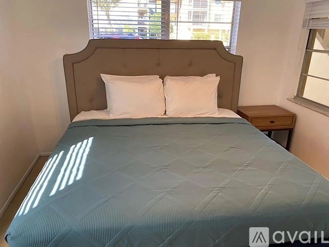A bed with a blue comforter and two white pillows in a room with a window.