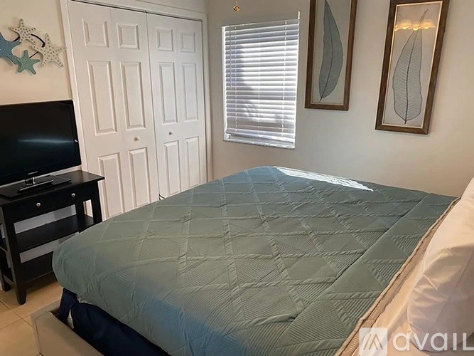 A bed with a blue and white comforter is in a room with a television and two framed pictures on the wall.