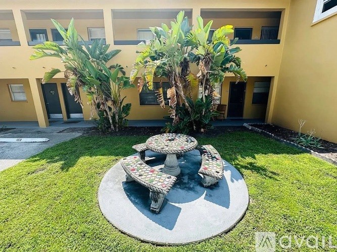 A round concrete table with a bench is in the middle of a grassy area.