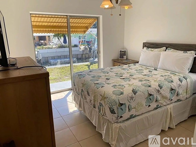 A bedroom with a bed, a television, and a sliding glass door leading to a backyard.