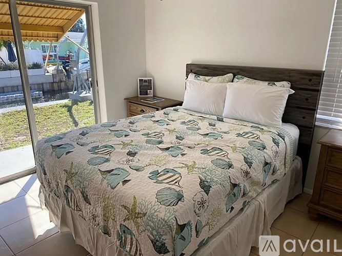 A bed with a leaf patterned comforter is in a room with a sliding glass door.