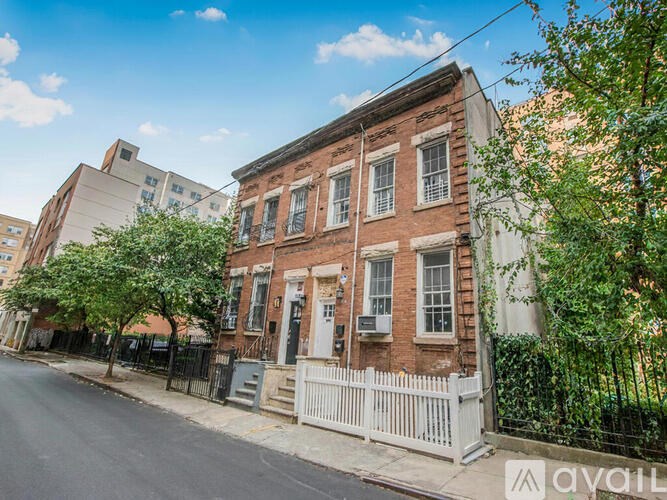 A row of old brick buildings with white fences line a quiet street.