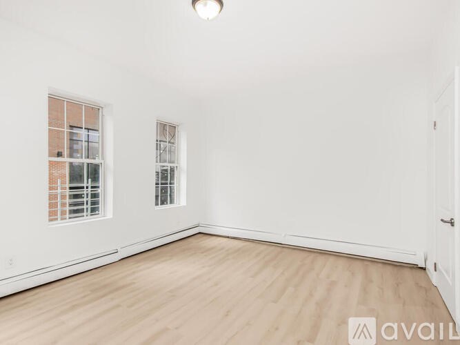 A room with wooden flooring and two windows.
