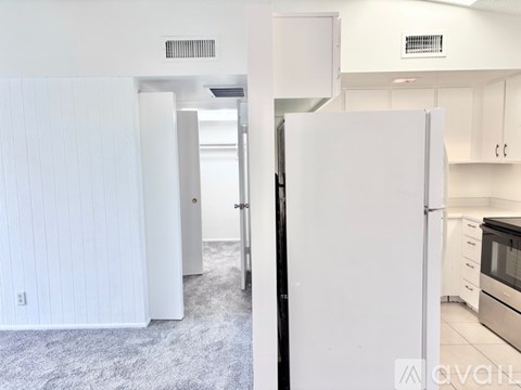 A white refrigerator is in the foreground of a kitchen.