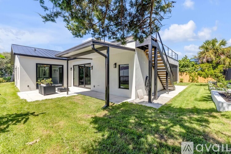 A modern house with a white exterior and a black roof is surrounded by a well-manicured lawn.
