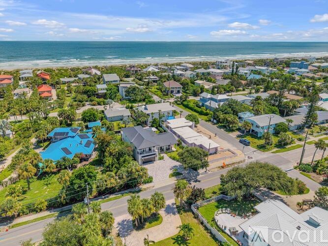 A bird's eye view of a residential area with houses, a swimming pool, and a beach in the distance.