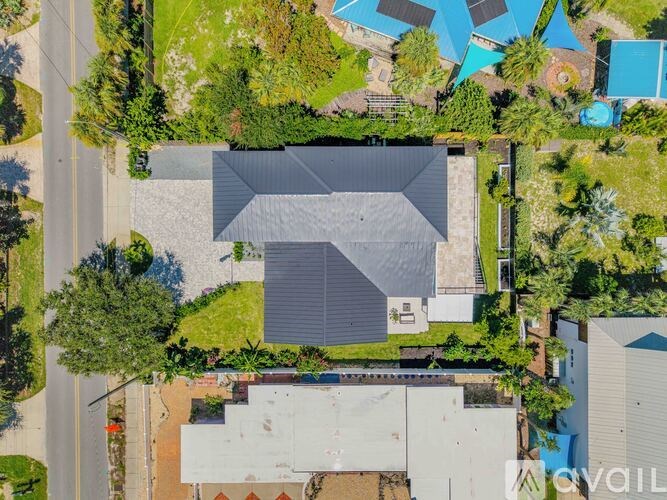 A house with a grey roof is surrounded by trees and a pool.