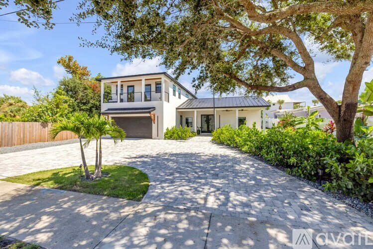 A modern house with a large driveway and a tree in front.