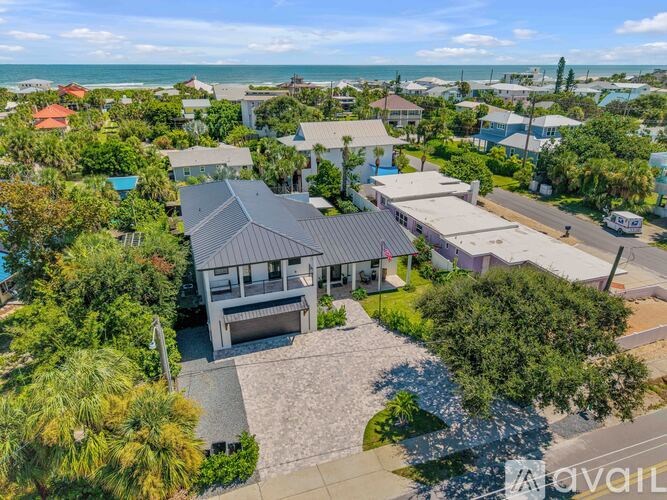 A house with a grey roof is surrounded by greenery and other houses.