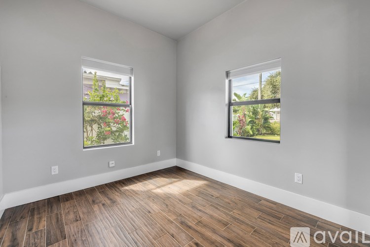 A room with wooden flooring and two windows with outdoor views.