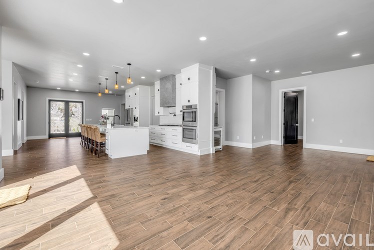 A spacious living room with wooden flooring and a kitchen area in the background.
