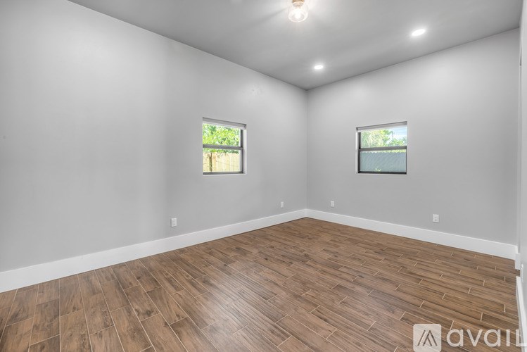 A room with wooden flooring and two windows.