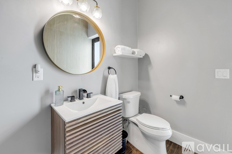 A bathroom with a round mirror, sink, toilet, and lights.