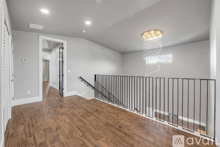 A well-lit room with wooden flooring and a staircase with a metal railing.