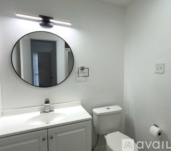 A bathroom with a toilet, sink, mirror, and light.