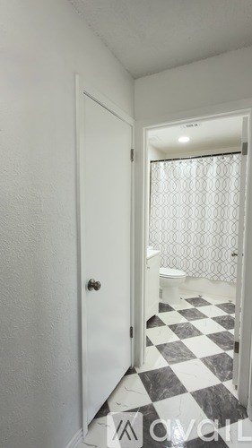 A white door is open to a bathroom with a black and white checkered floor.