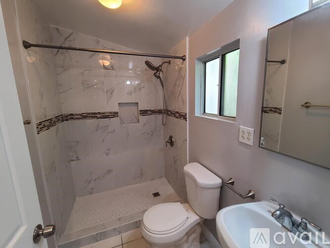 A white toilet is in a marble bathroom with a walk-in shower.