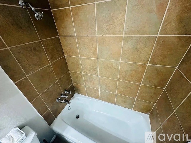 A white bathtub is in a bathroom with brown tiles.